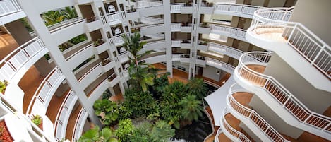 Un atrio de varios niveles con balcones, plantas de interior y una fuente central.