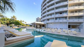 A hotel pool area with sun loungers and a large building with balconies.