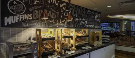 A bakery counter with a variety of baked goods and a chalkboard menu listing items like Danish croissants, muffins, and gluten-free options.