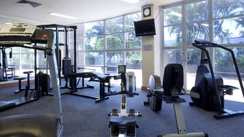 A gym with various exercise equipment, large windows, and a clock on the wall.