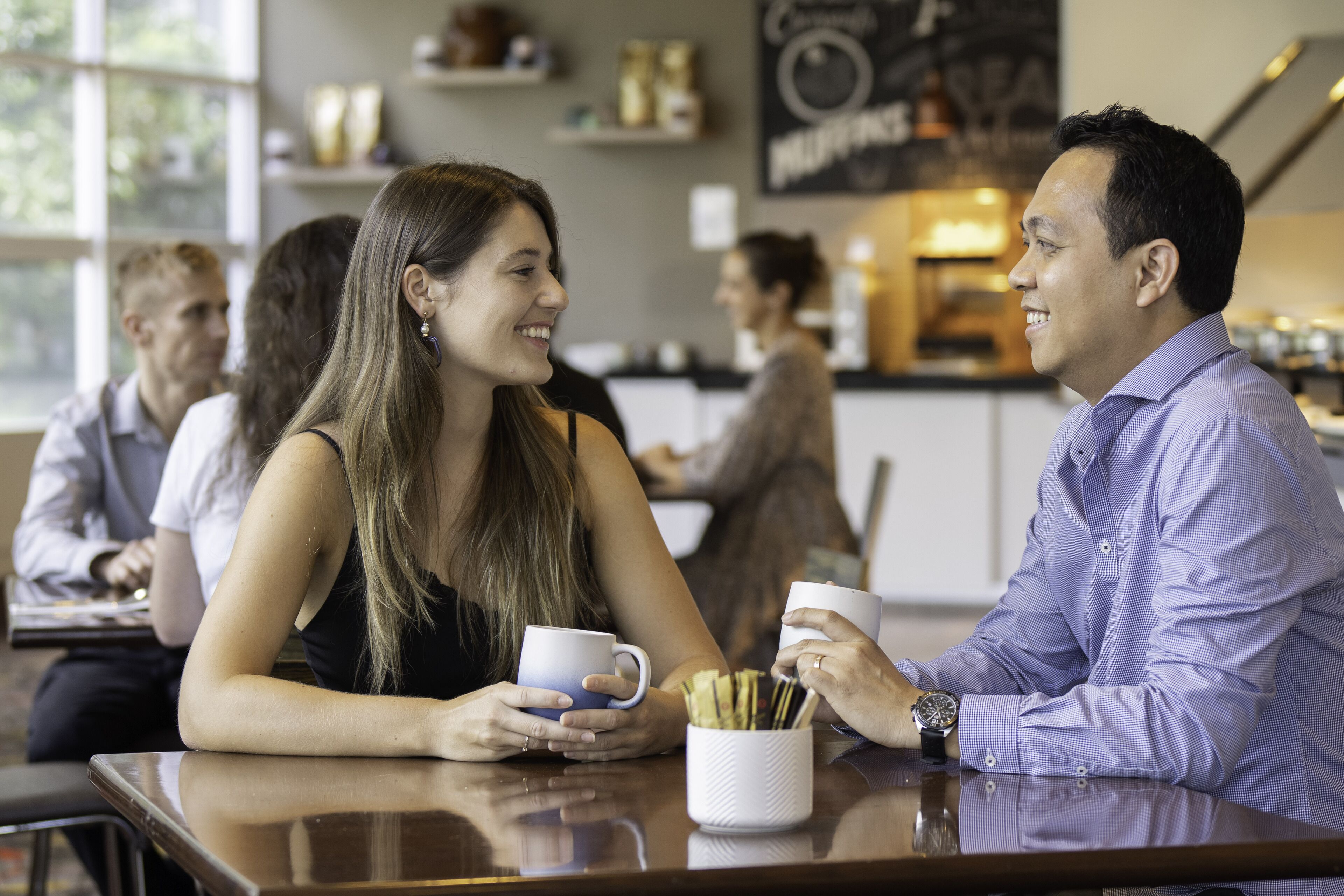 A cafe setting with tables and chairs, a coffee machine, and a menu board in the background.