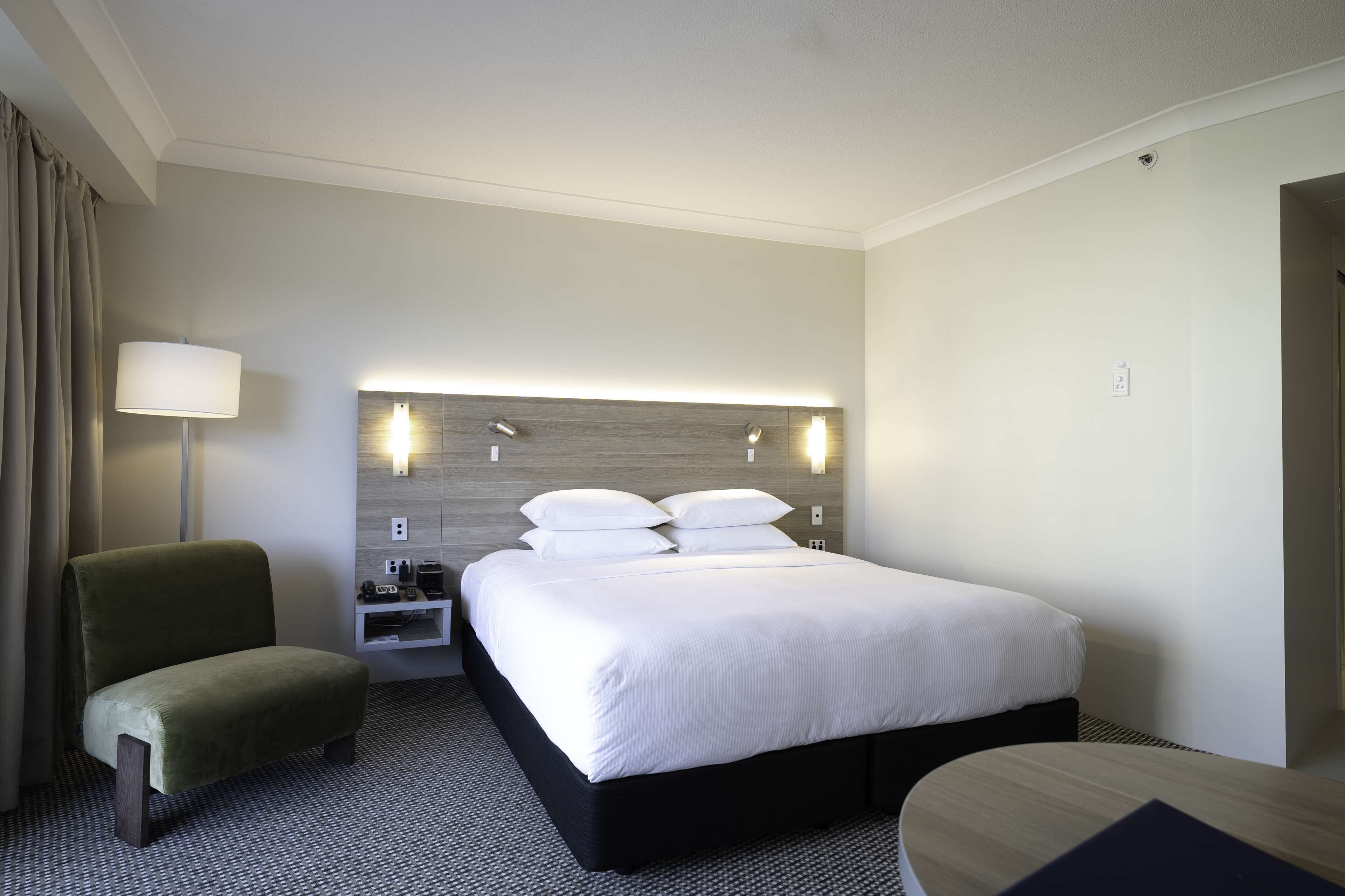 A hotel room with a large bed, a bedside table, a lamp, and a chair.