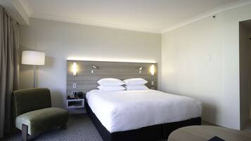 A hotel room with a large bed, a bedside table, a lamp, and a chair.