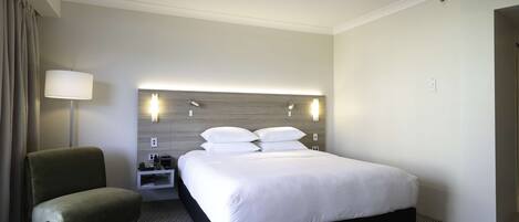 A hotel room with a large bed, a bedside table, a lamp, and a chair.
