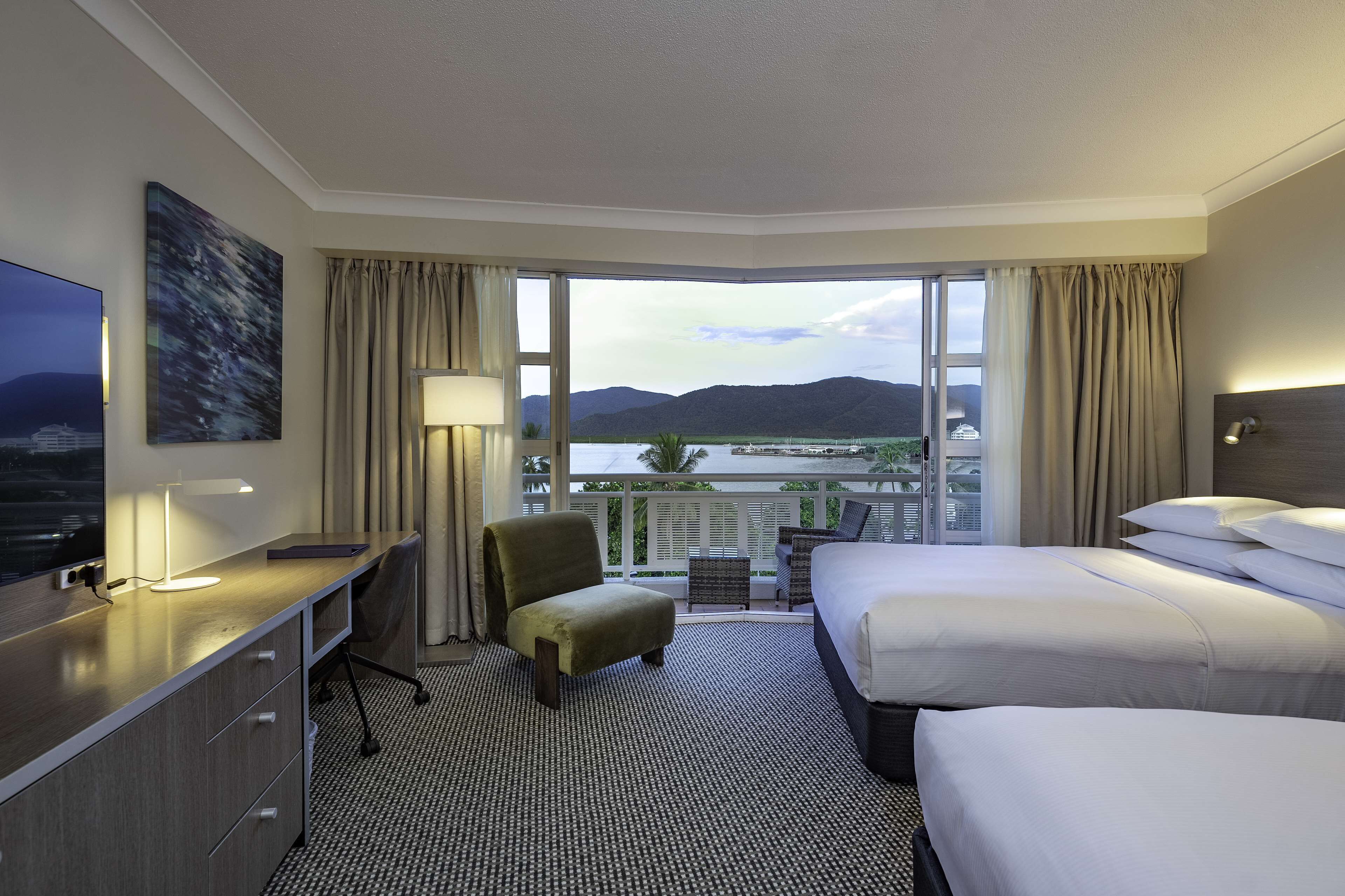 Ein Hotelzimmer mit einem großen Bett, einem Schreibtisch mit Stuhl, einem Fernseher und Blick auf ein Gewässer und Berge.