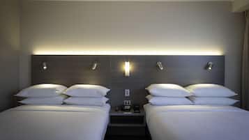 A hotel room with two beds, a nightstand, a wall-mounted light, and a power outlet.