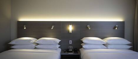 A hotel room with two beds, a nightstand, a wall-mounted light, and a power outlet.