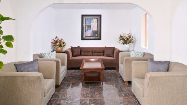 A living room with a brown sofa, beige armchairs, a wooden coffee table, and a framed abstract painting on the wall. - Americas Best Value Inn Clute Lake Jackson (Clute)