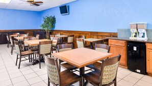A restaurant with wooden tables and chairs, a kitchen area, and a ceiling fan. - Americas Best Value Inn Clute Lake Jackson (Clute)