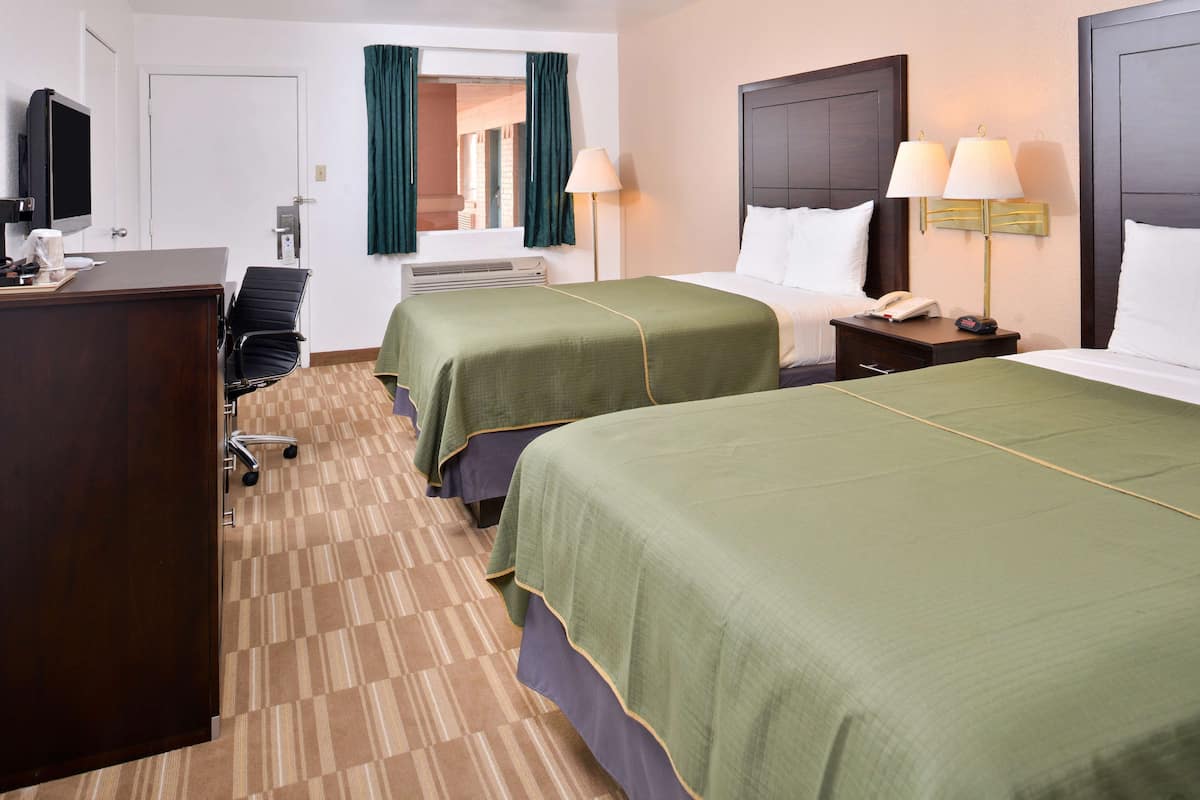Une chambre d’hôtel avec deux lits, un bureau avec un ordinateur, une chaise et un téléviseur.