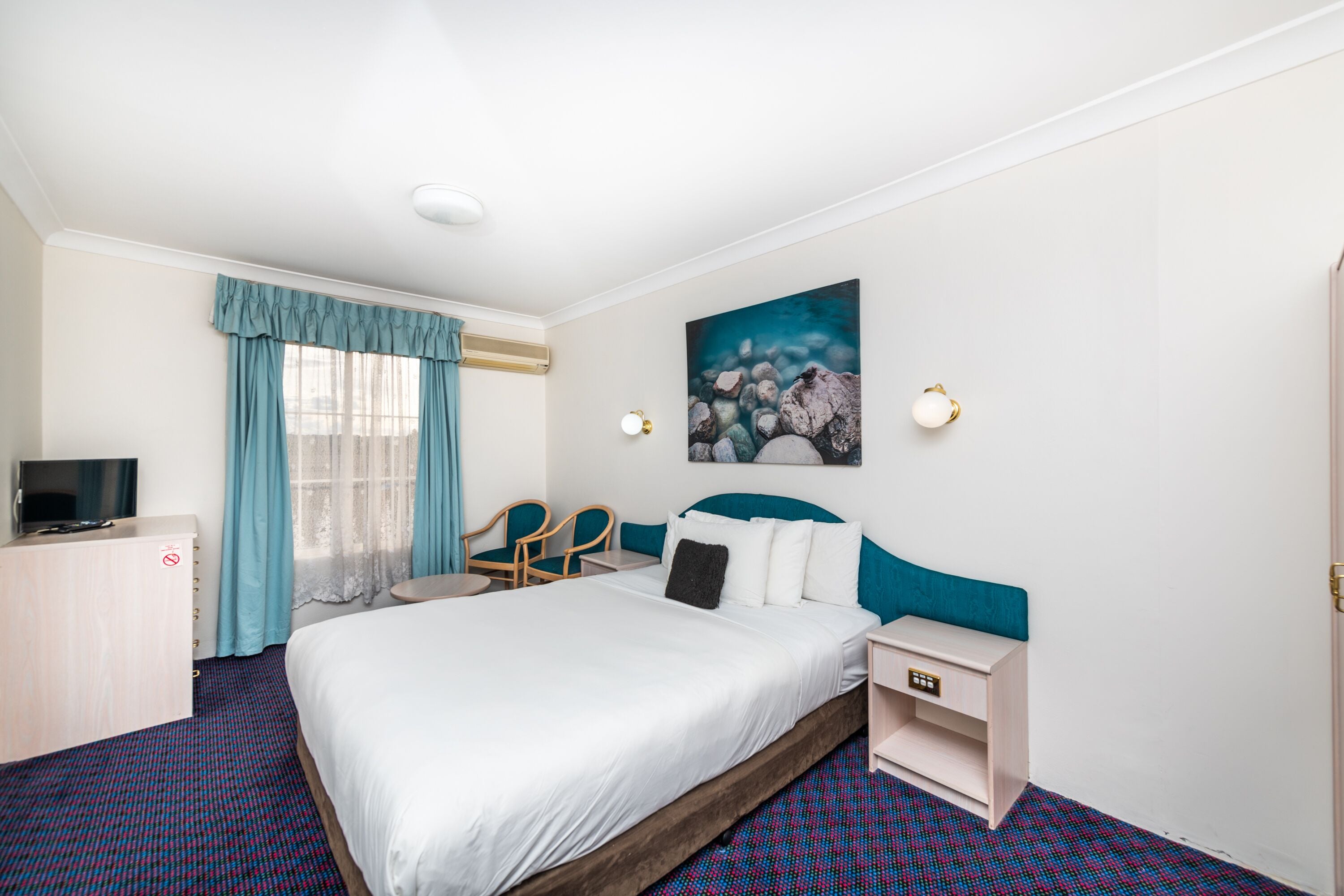 Habitación de hotel con una cama grande, un escritorio con televisión, una silla y un cuadro en la pared.
