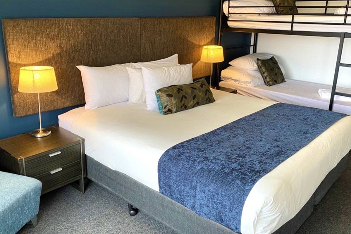 Uma cama de solteiro com um cobertor azul, duas luminárias de cabeceira, uma cabeceira e uma cama beliche em cima.