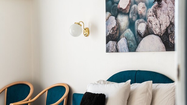 A modern bedroom with a bed, two chairs, a wall-mounted light, and a painting of rocks. - Golden Age Motor Inn Queanbeyan (Queanbeyan East)