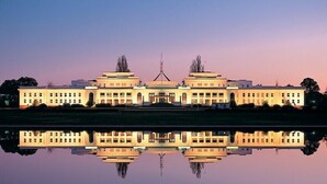A large, symmetrical building with a central tower and two symmetrical wings, reflecting in a calm body of water. - Golden Age Motor Inn Queanbeyan (Queanbeyan East)