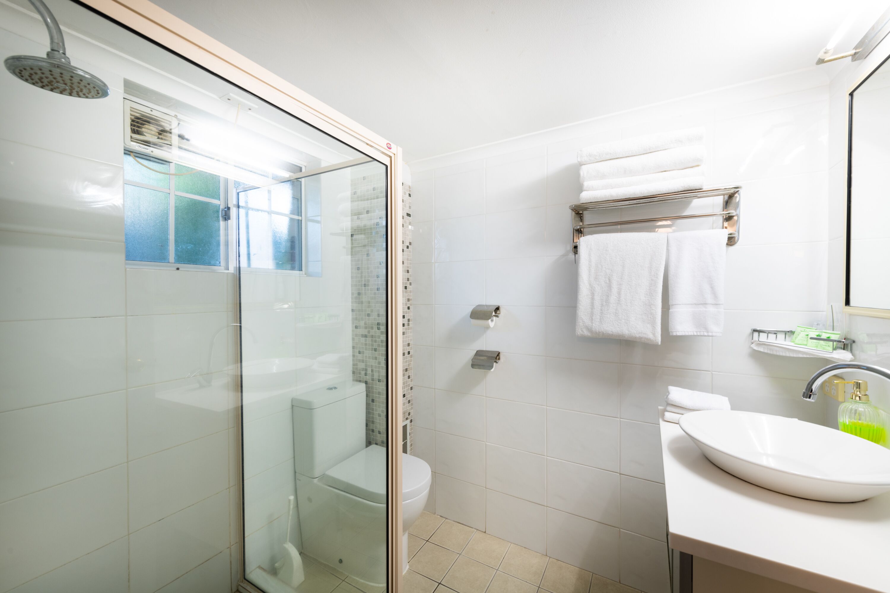 A modern bathroom with a glass-enclosed shower, a white toilet, a sink with a mirror, and a towel rack with two towels.
