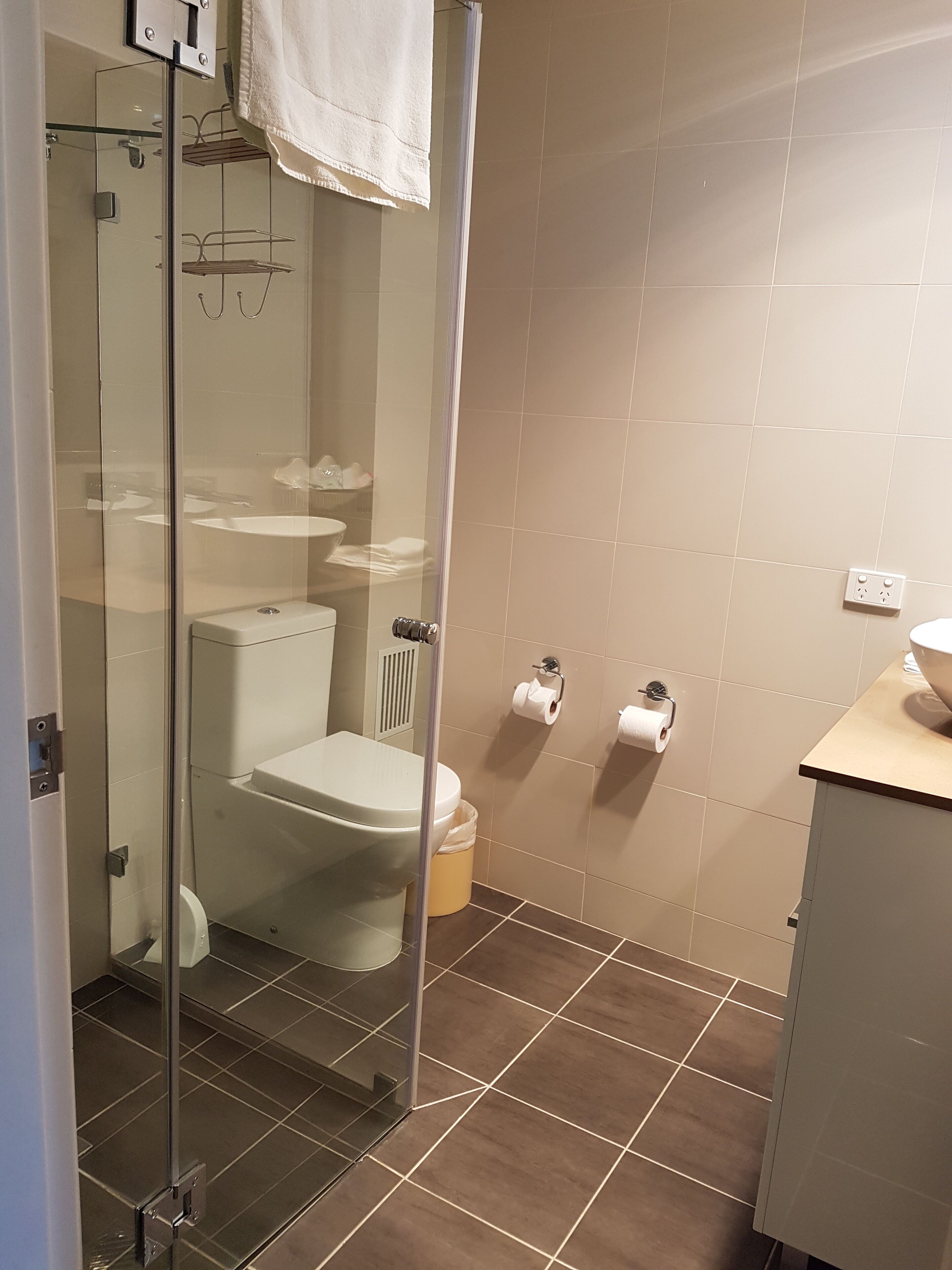 Un baño con cabina de ducha de vidrio, un inodoro, un lavamanos y dos rollos de papel higiénico en la pared.