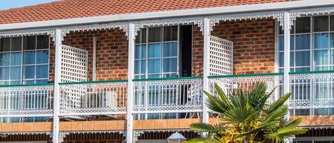 A two-story building with a red-tiled roof, white balconies with intricate lattice designs, and a brick facade.