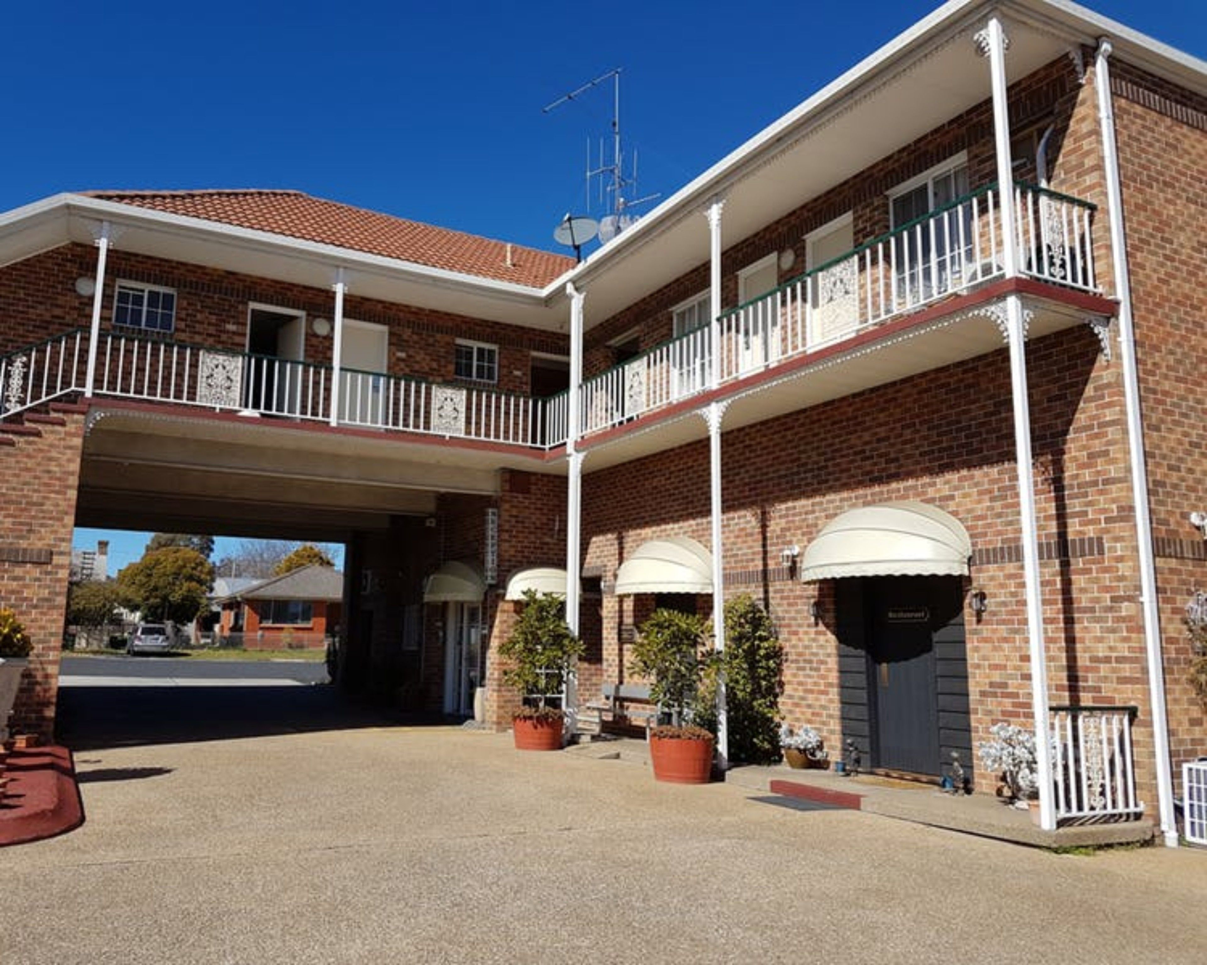 Un edificio a due piani con un ingresso coperto, pareti in mattoni e un balcone con ringhiere bianche.