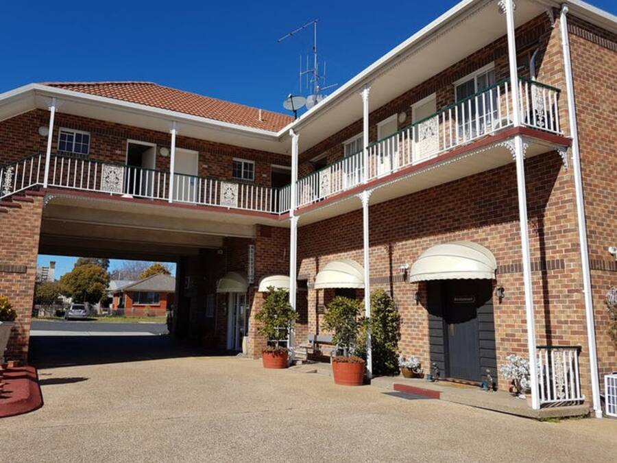 Un edificio a due piani con un ingresso coperto, pareti in mattoni e un balcone con ringhiere bianche.