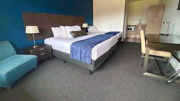 A hotel room with a bed, a desk, a chair, a nightstand, and a lamp.
