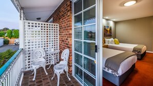 A balcony with white lattice and two white chairs, a brick wall, and a room with two beds and a painting. - Golden Age Motor Inn Queanbeyan (Queanbeyan East)