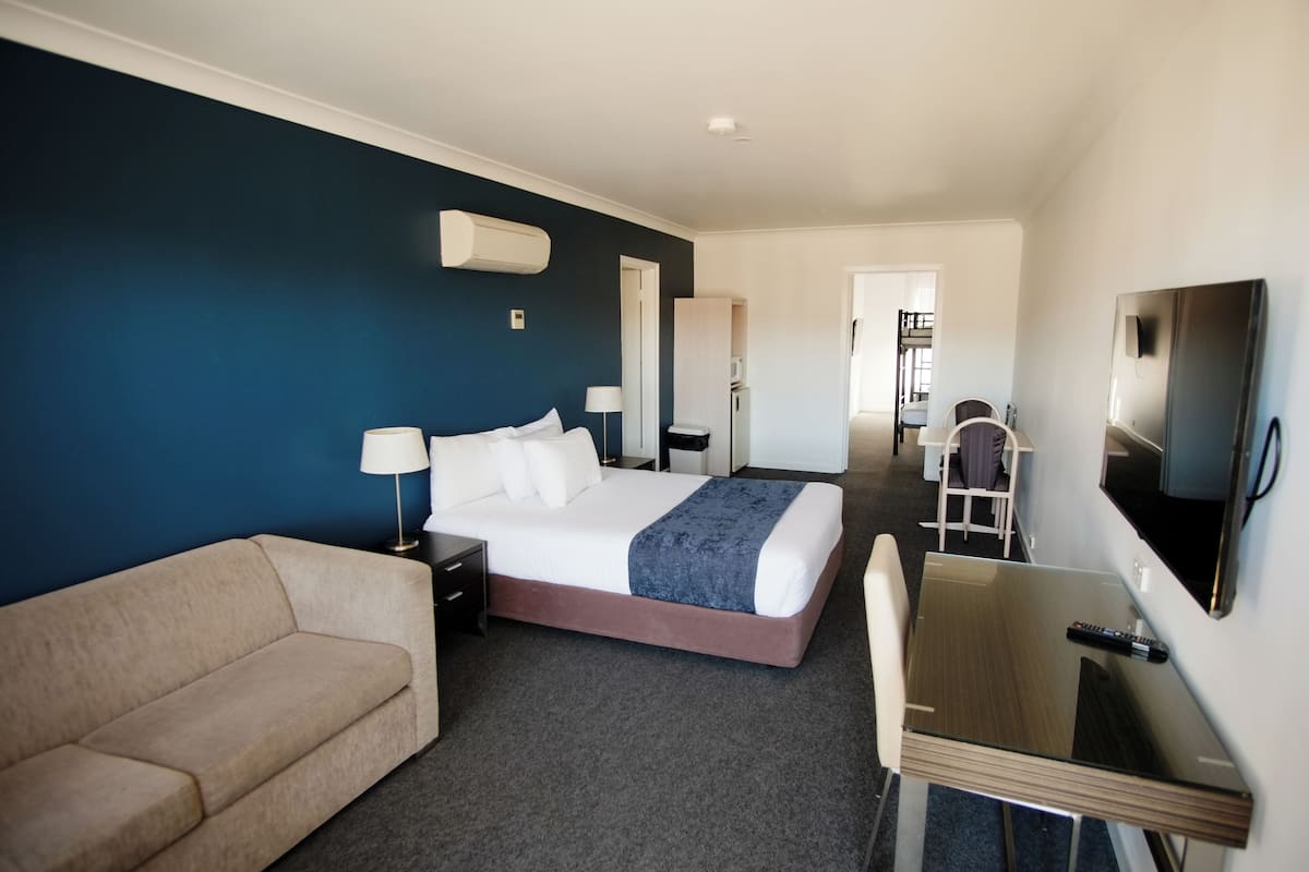 Quarto de hotel com cama, escrivaninha, cadeira e televisão.