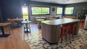 Un interior moderno con una zona de bar, varias opciones de asientos y amplios ventanales que dejan entrar la luz natural.
