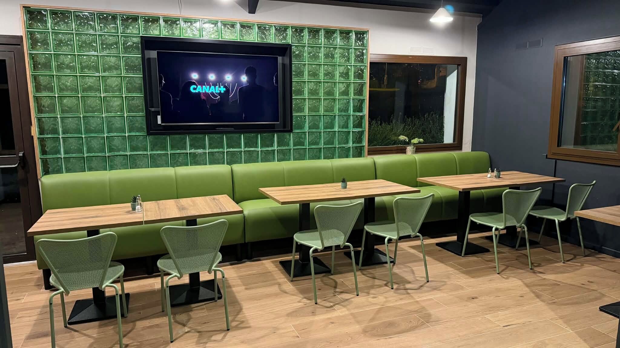 A restaurant interior with green seating, wooden tables, and a TV screen displaying 'CANAL+'.