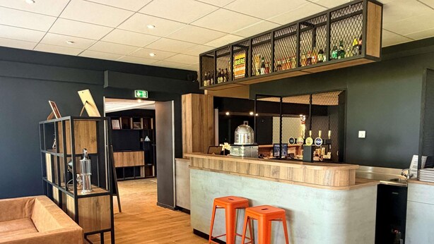 Zona de bar moderna con taburetes, barra y exhibición de botellas.
