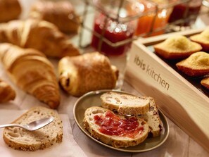 A breakfast buffet with croissants, sliced bread with jam, and a sign that reads 'ibis kitchen'. - ibis Dieppe Val Druel (Dieppe)