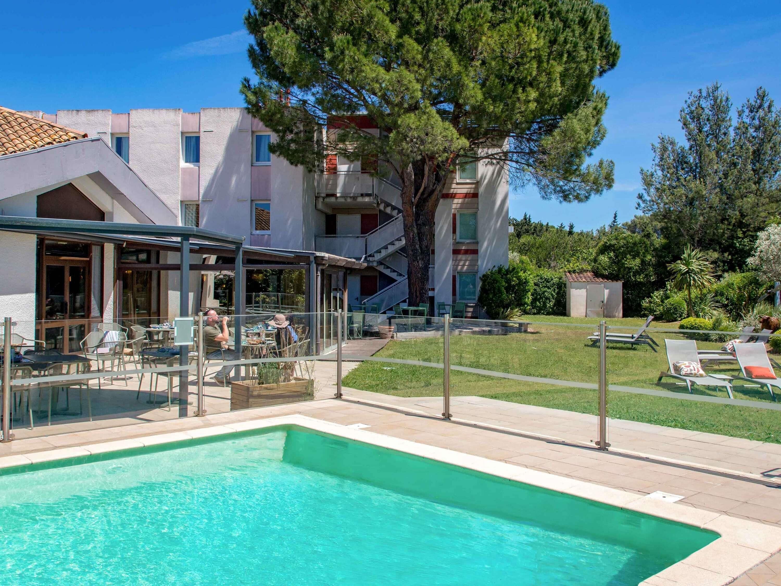 Un espace piscine avec des chaises longues, un coin salon abrité et un bâtiment doté d’un escalier.