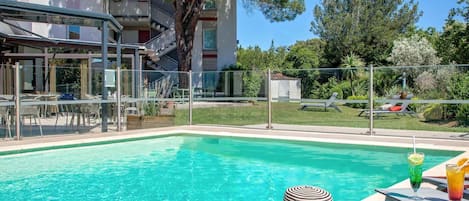 Una piscina al aire libre, sombrillas, sillones reclinables de piscina