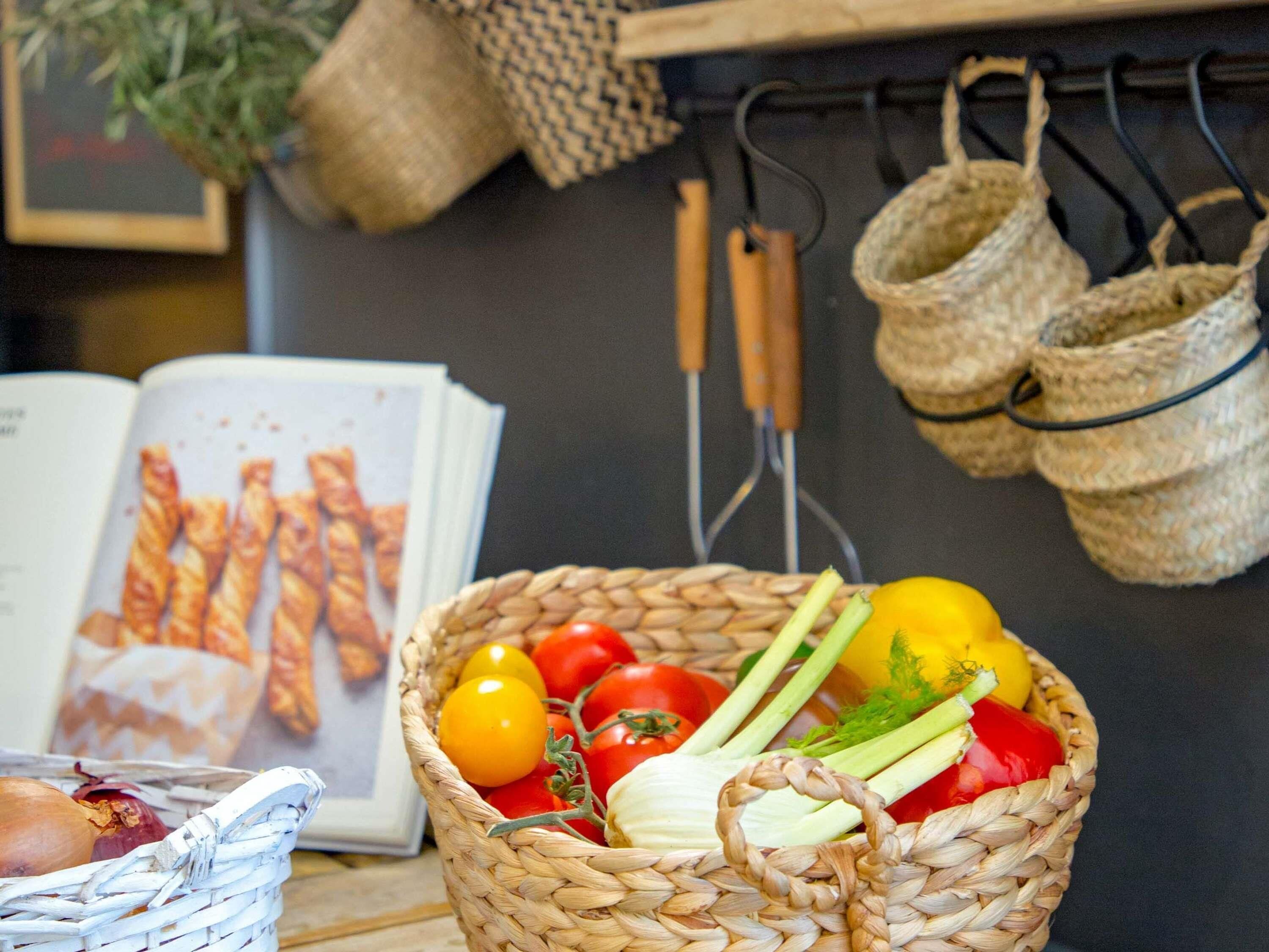 Un panier contenant des légumes, un livre et des ustensiles de cuisine.