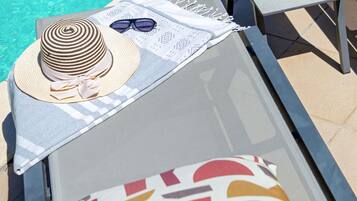 Un espace de détente au bord de la piscine, avec une serviette à rayures, un chapeau et des lunettes de soleil posés sur une chaise longue.
