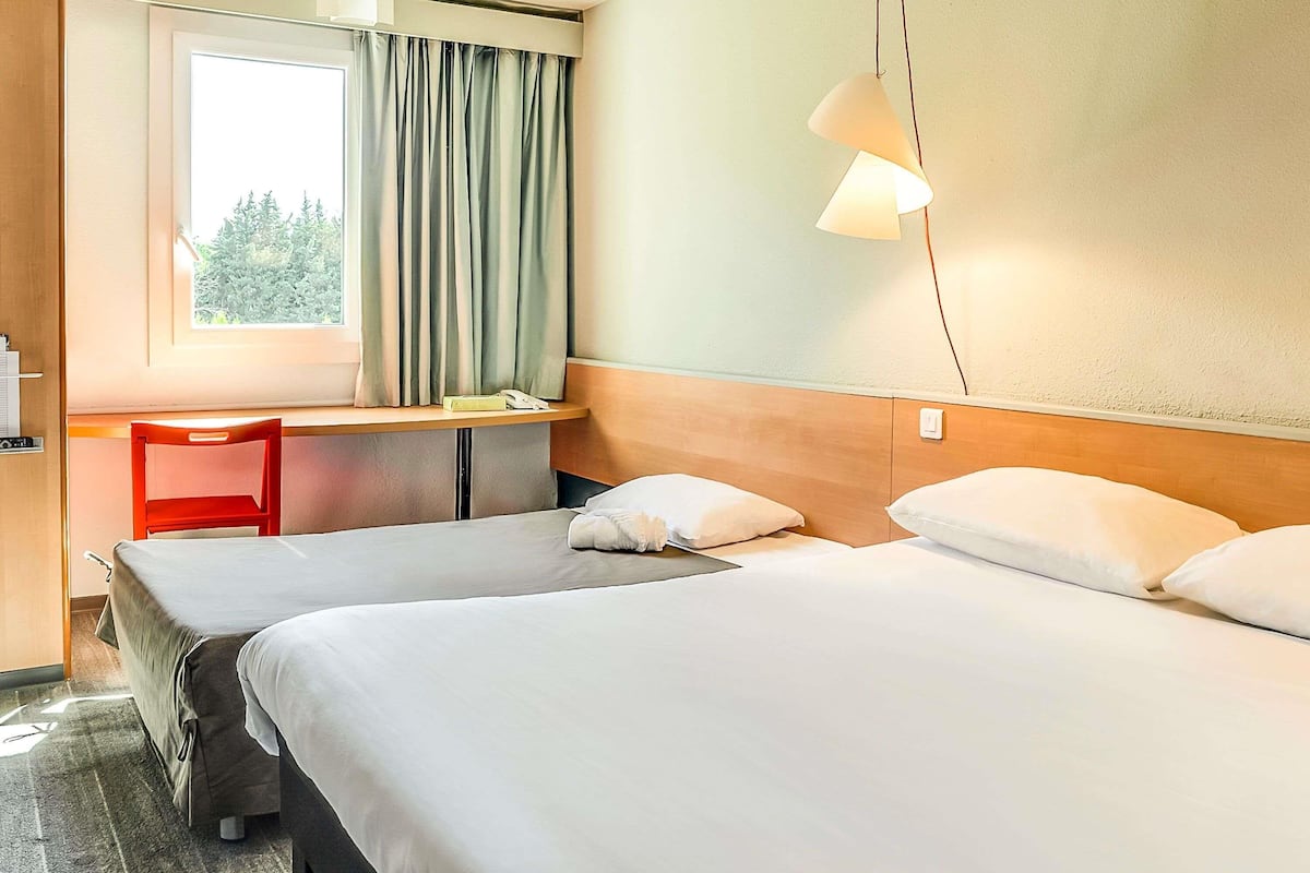 Une chambre d’hôtel avec deux lits, un bureau, une chaise et une fenêtre avec des rideaux.