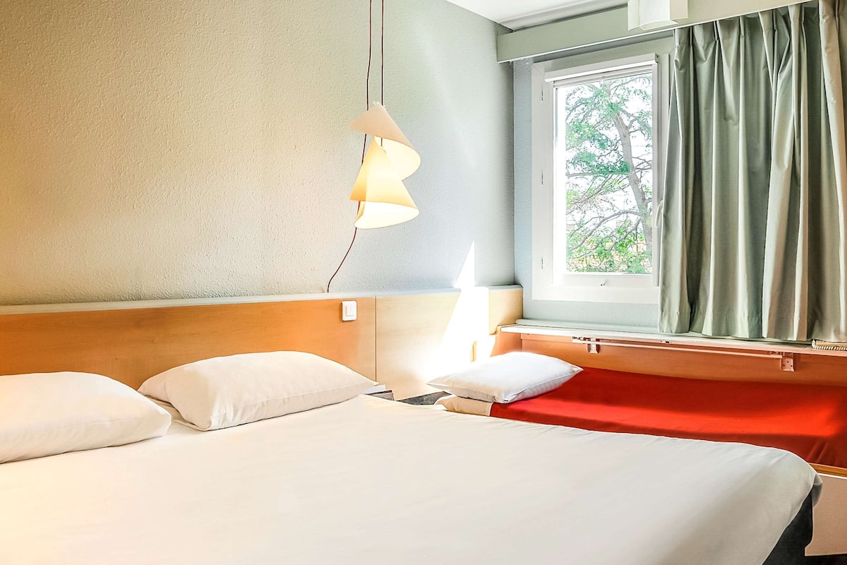 Relax in comfort with a large bed, bedside table, and a window offering a view of lush greenery.