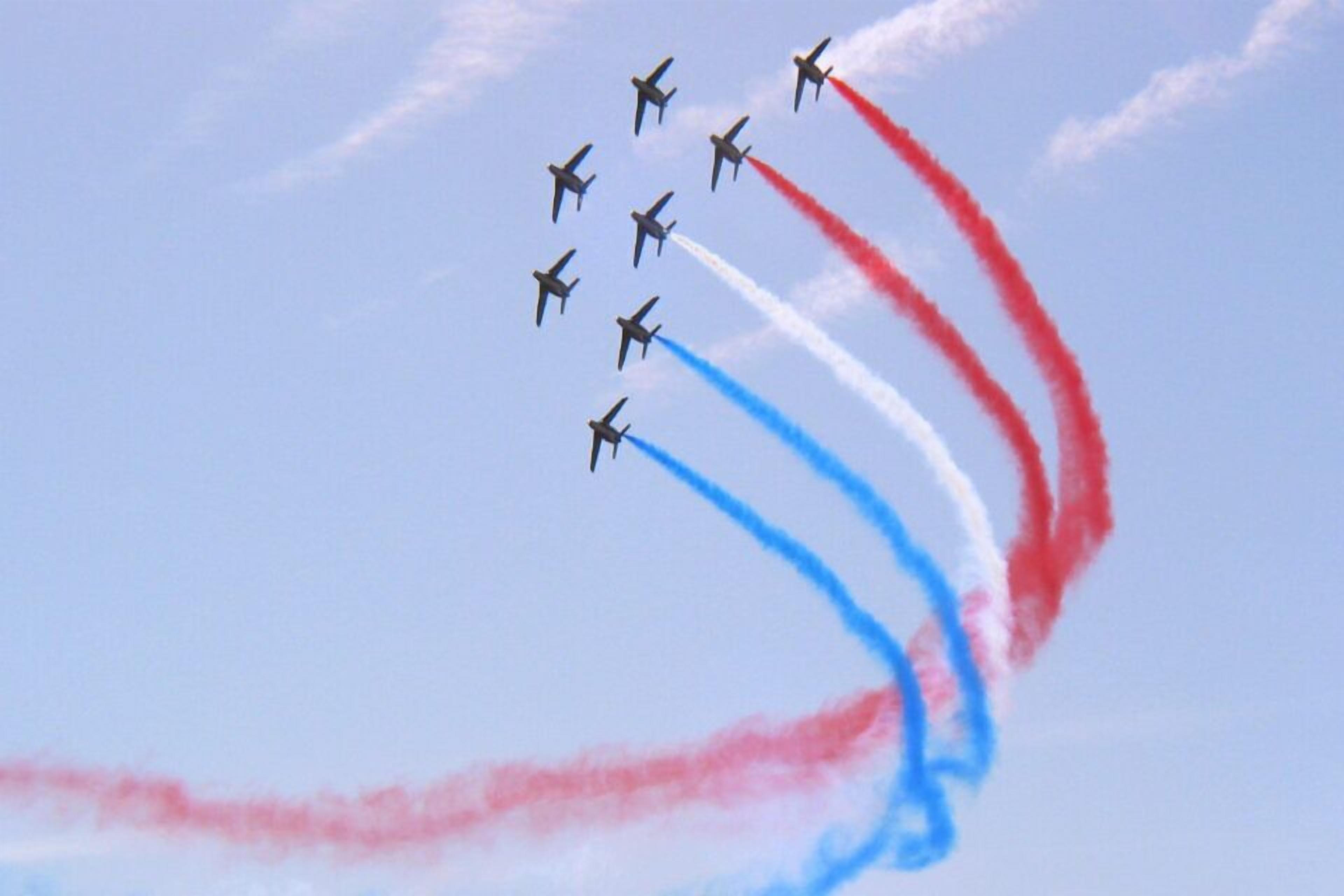 A group of jets performing an aerial maneuver with red, white, and blue smoke trails.
