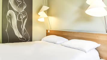 Una habitación de hotel con una cama, almohadas blancas, un cabecero de madera, una obra de arte en la pared y dos lámparas colgantes.