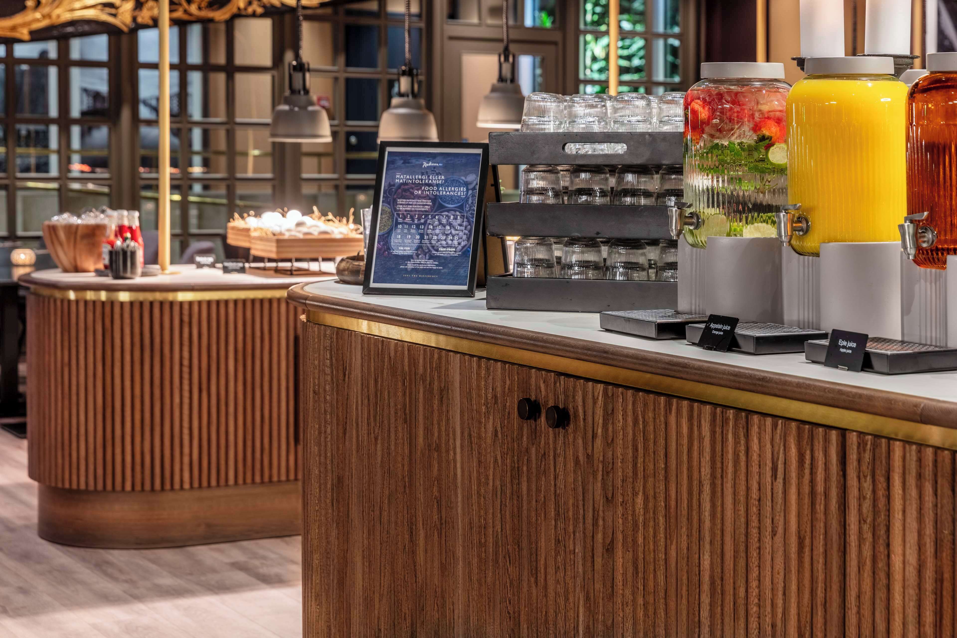 A hotel reception area with a wooden counter, a coffee machine, and beverage dispensers.