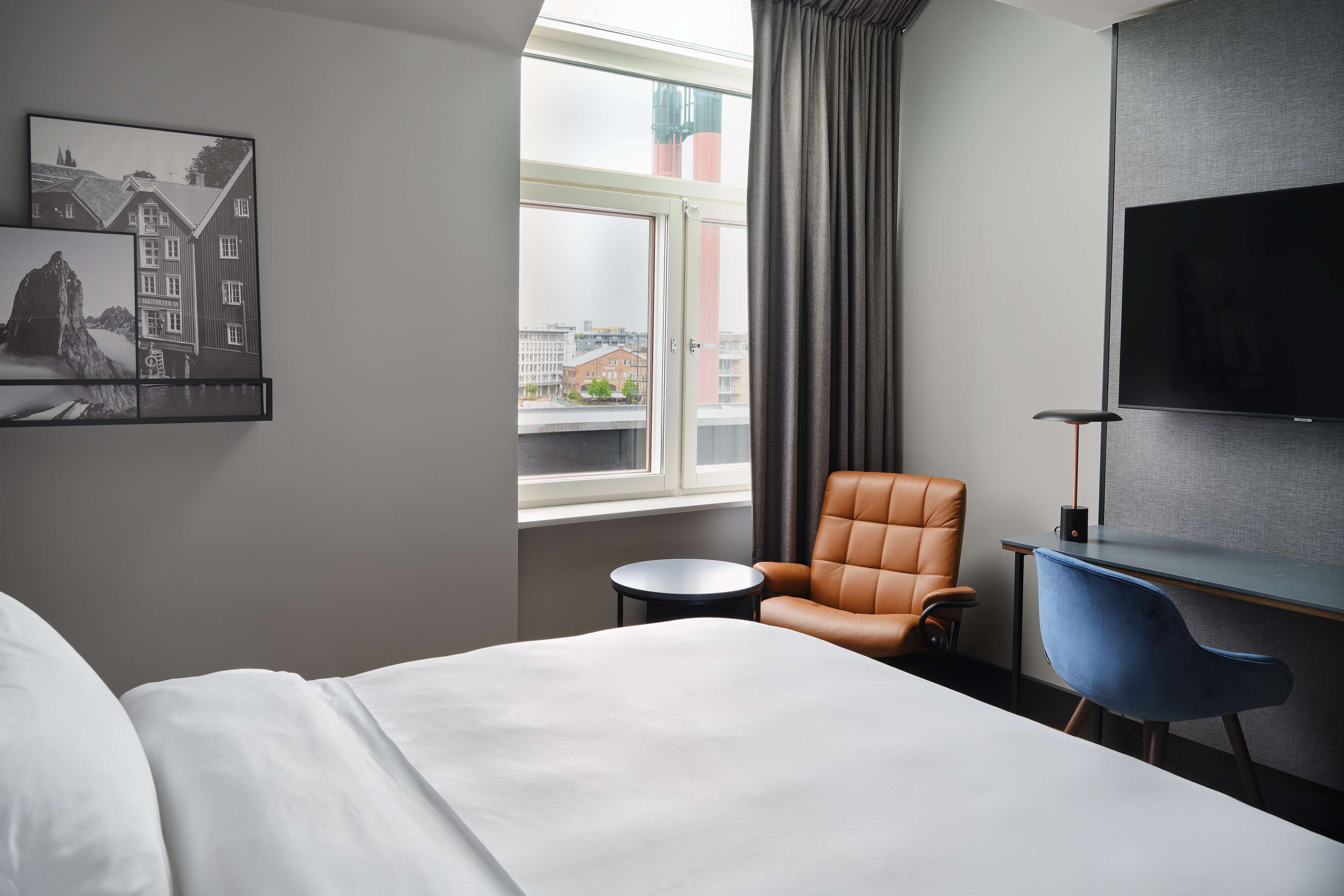 A hotel room with a bed, a desk with a chair, a television, and a window with curtains.