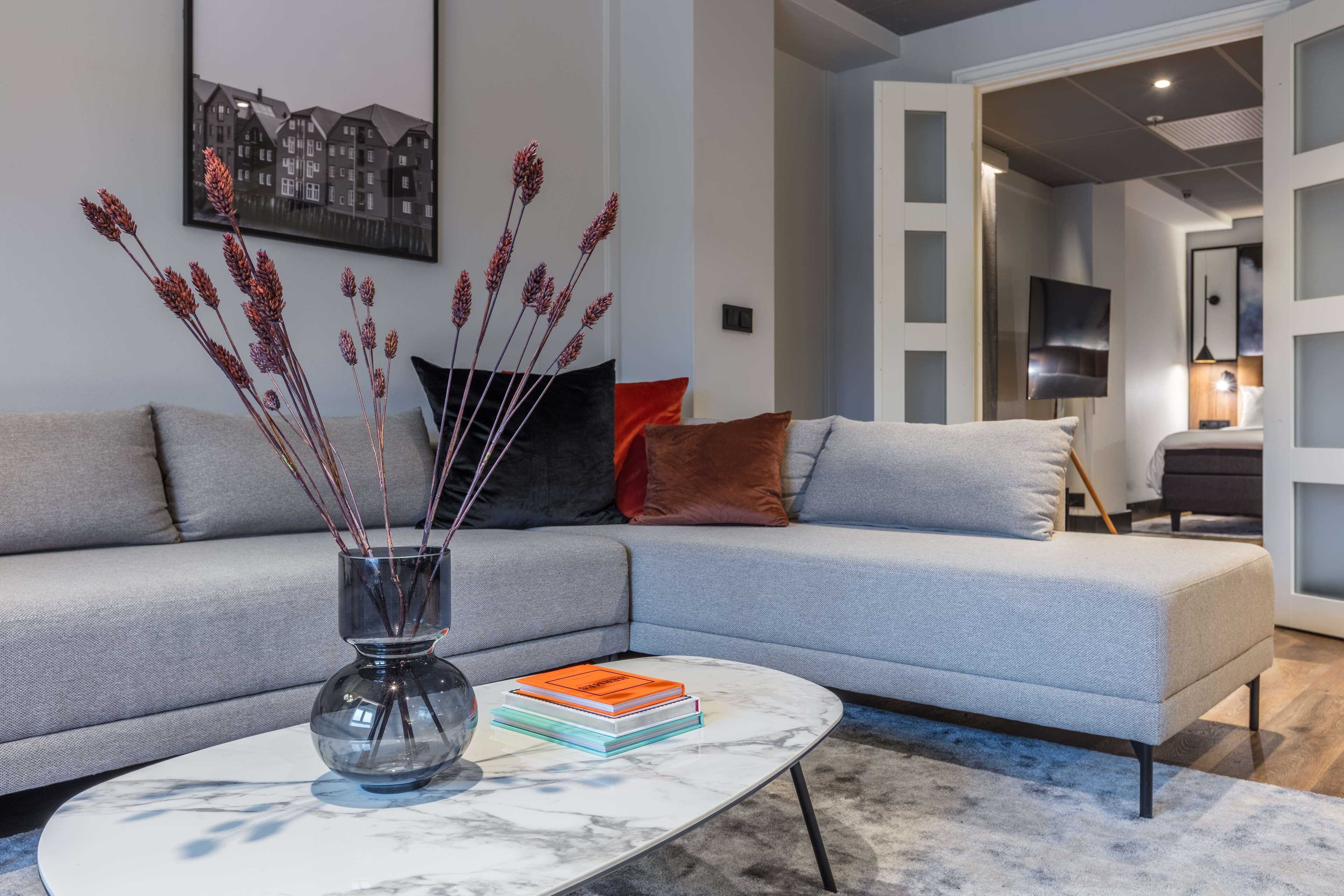 A modern living room with a grey sofa, a marble coffee table, and a vase with dried plants.