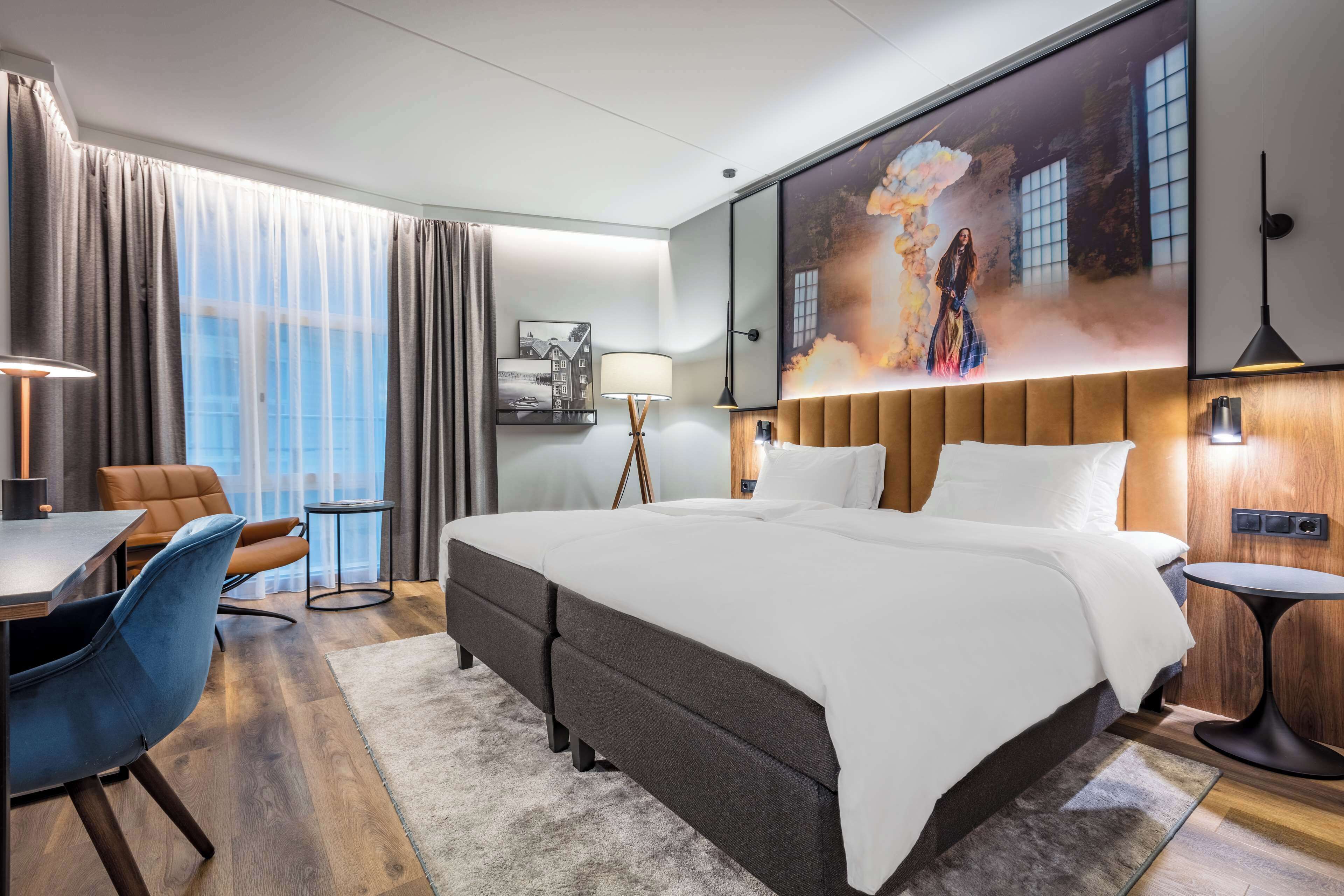 Ein modernes Hotelzimmer mit einem großen Bett, einem Schreibtisch, einem Stuhl und einem Bild an der Wand.