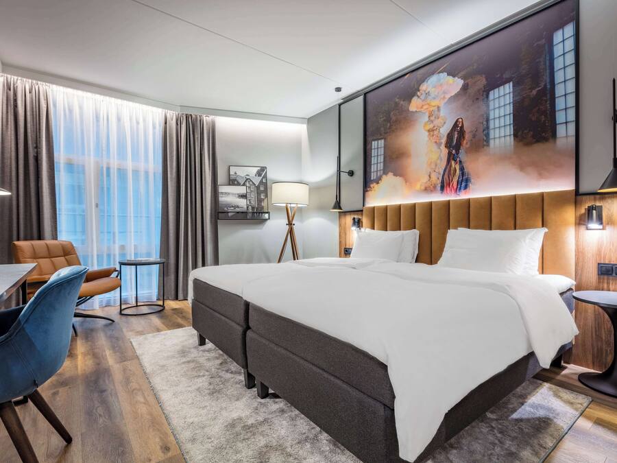 Et moderne hotelværelse med en stor seng, et skrivebord, en stol og et billede på væggen.