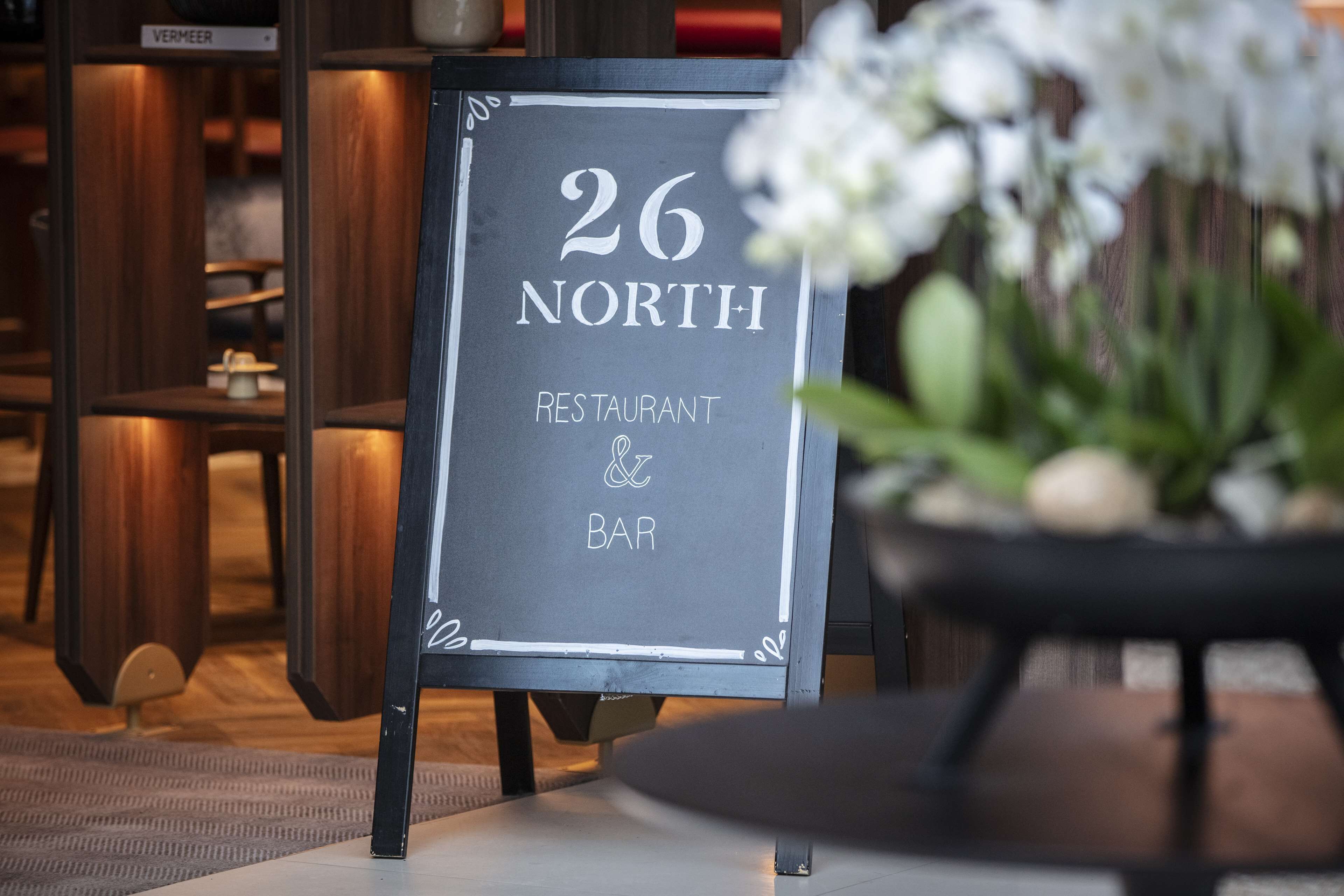 Ein Schild für '26 NORTH RESTAURANT & BAR' mit unscharfem Hintergrund von Sitzplätzen im Innenbereich.