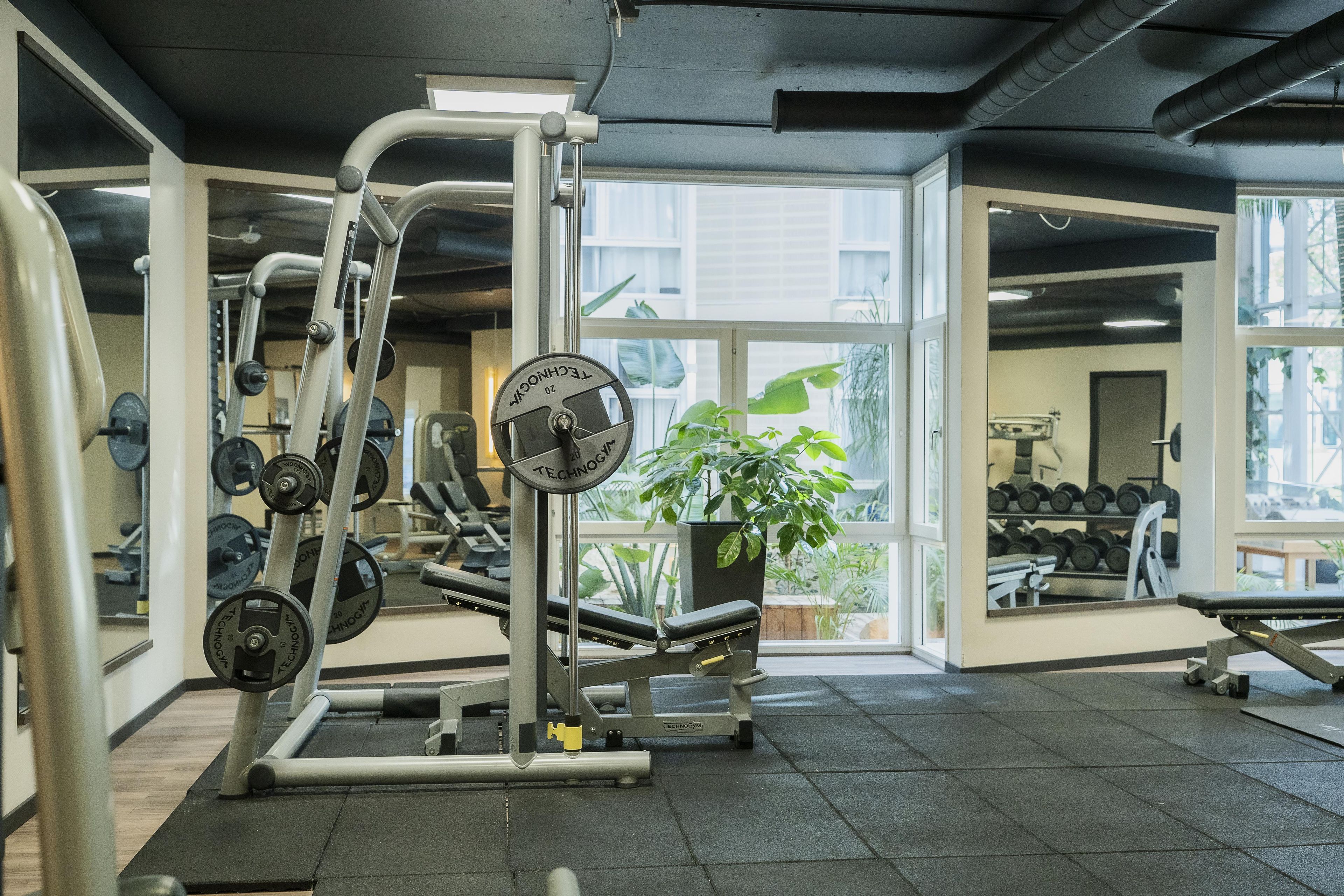A gym with exercise equipment, a mirror, and a window with a view of buildings.