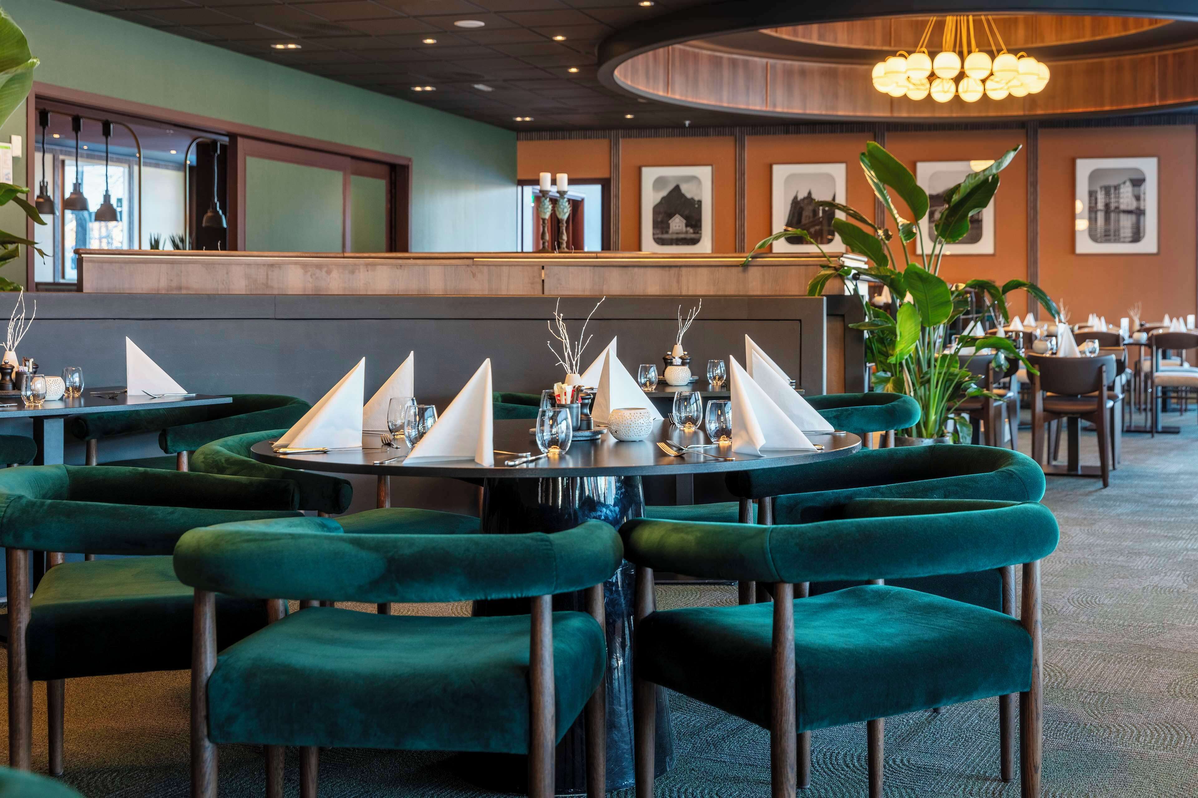 A restaurant with round tables, green upholstered chairs, and a modern interior design.