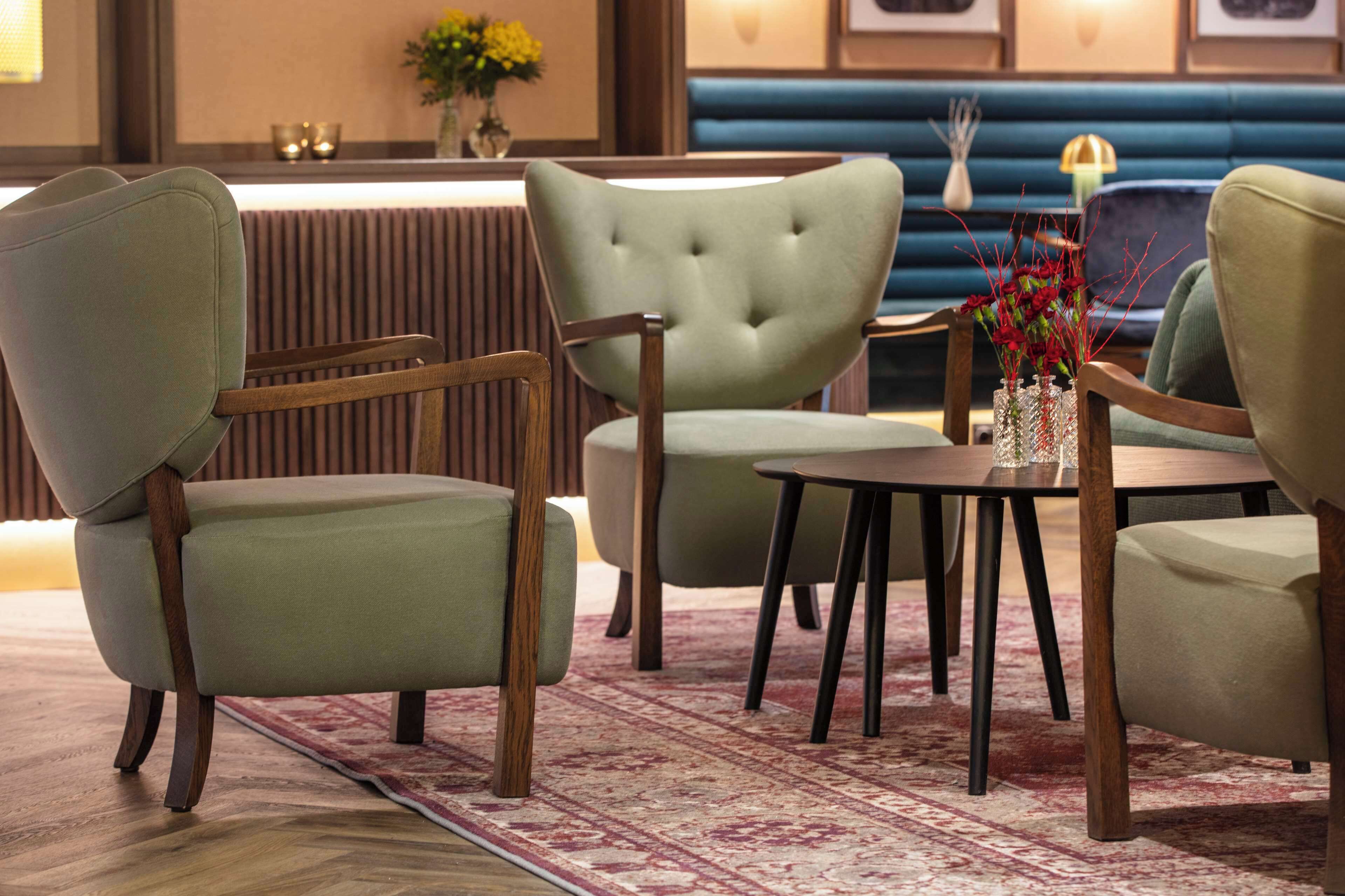 A seating area with upholstered chairs and a table, a patterned rug, and a decorative vase with flowers.