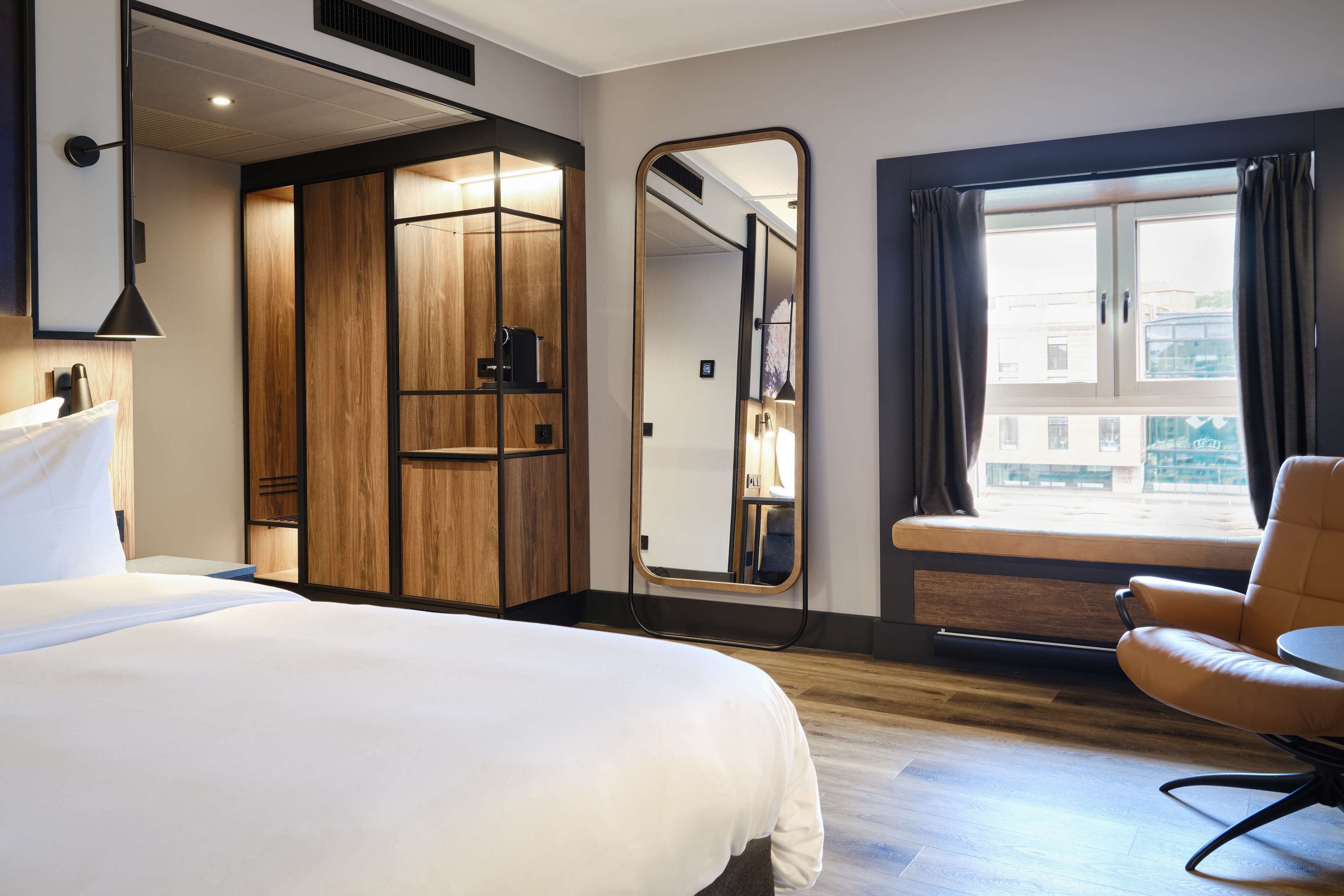 Een hotelkamer met een groot bed, een zithoek, een kledingkast en een raam met gordijnen.