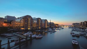 Un puerto deportivo con barcos amarrados, un edificio de cristal con ventanas iluminadas y una masa de agua tranquila que refleja el cielo.