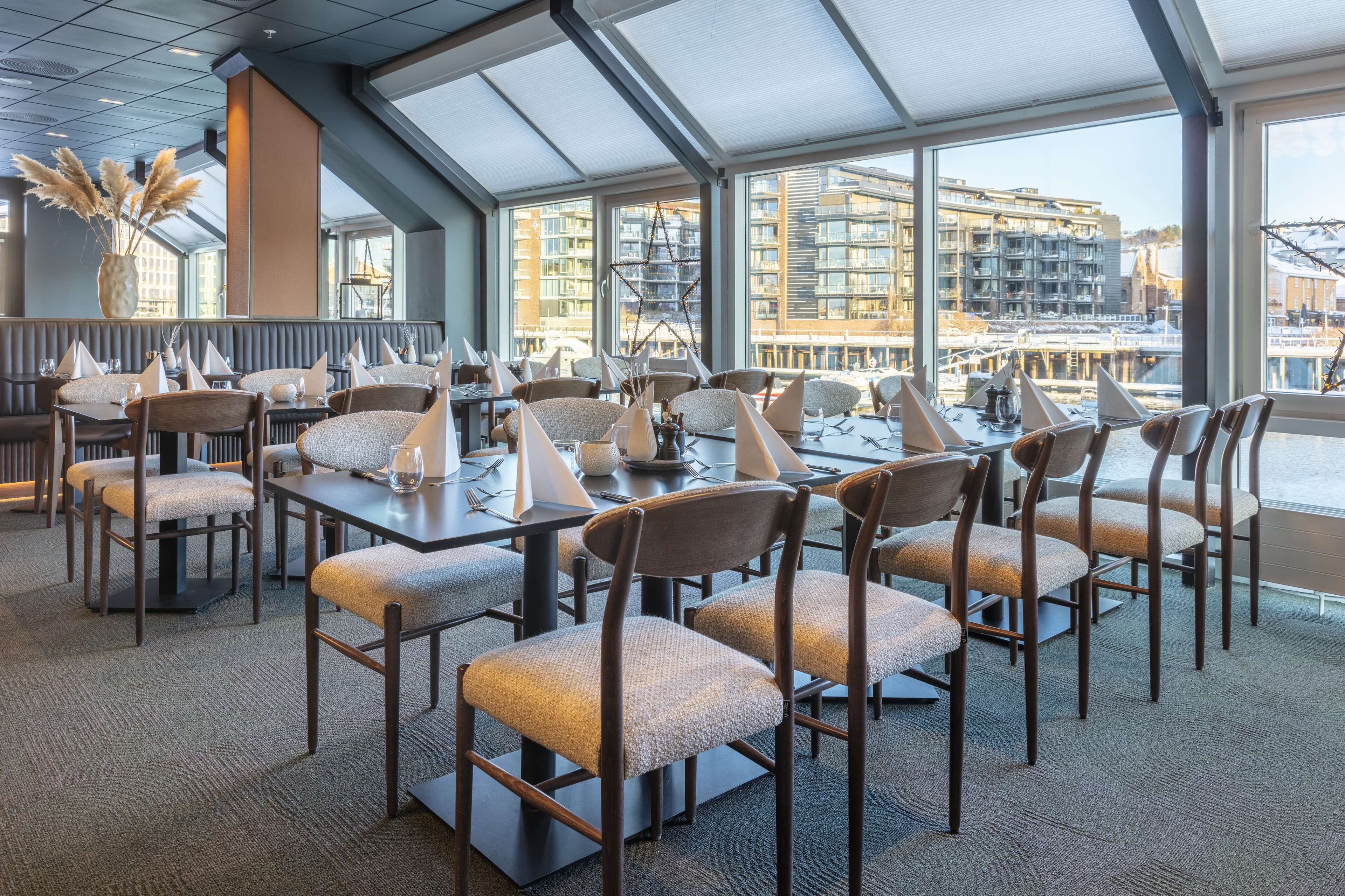 A modern dining area with high tables and chairs, large windows offering a view of the cityscape.